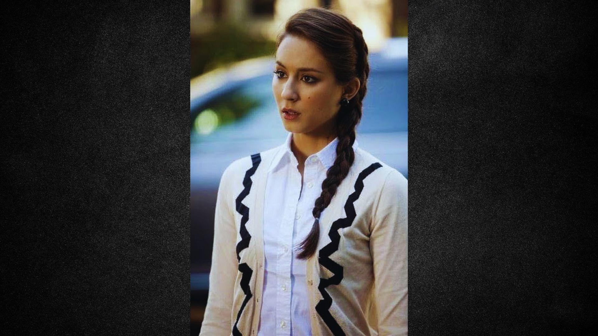 A woman with braided hair wearing a white shirt, smiling and looking towards the camera.