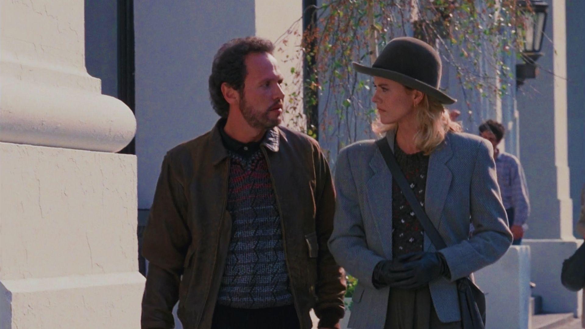 A man and woman stand side by side on a city street, both smiling and dressed casually.