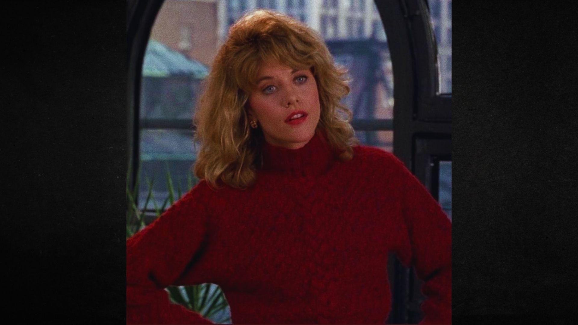 A woman in a red sweater stands by a window, looking out at the view beyond.