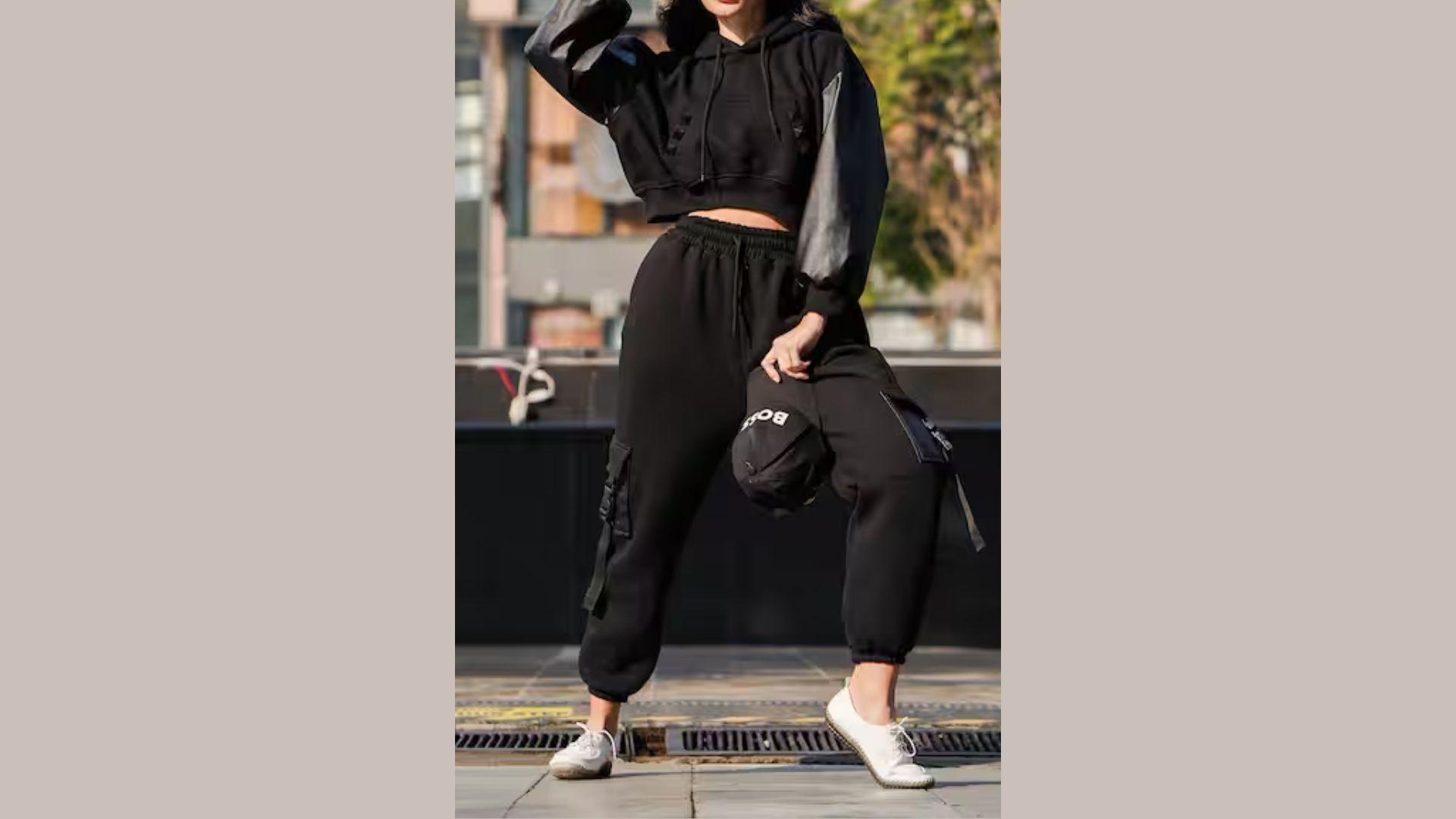 A woman wearing black pants and a hoodie stands confidently, showcasing a casual and comfortable style.