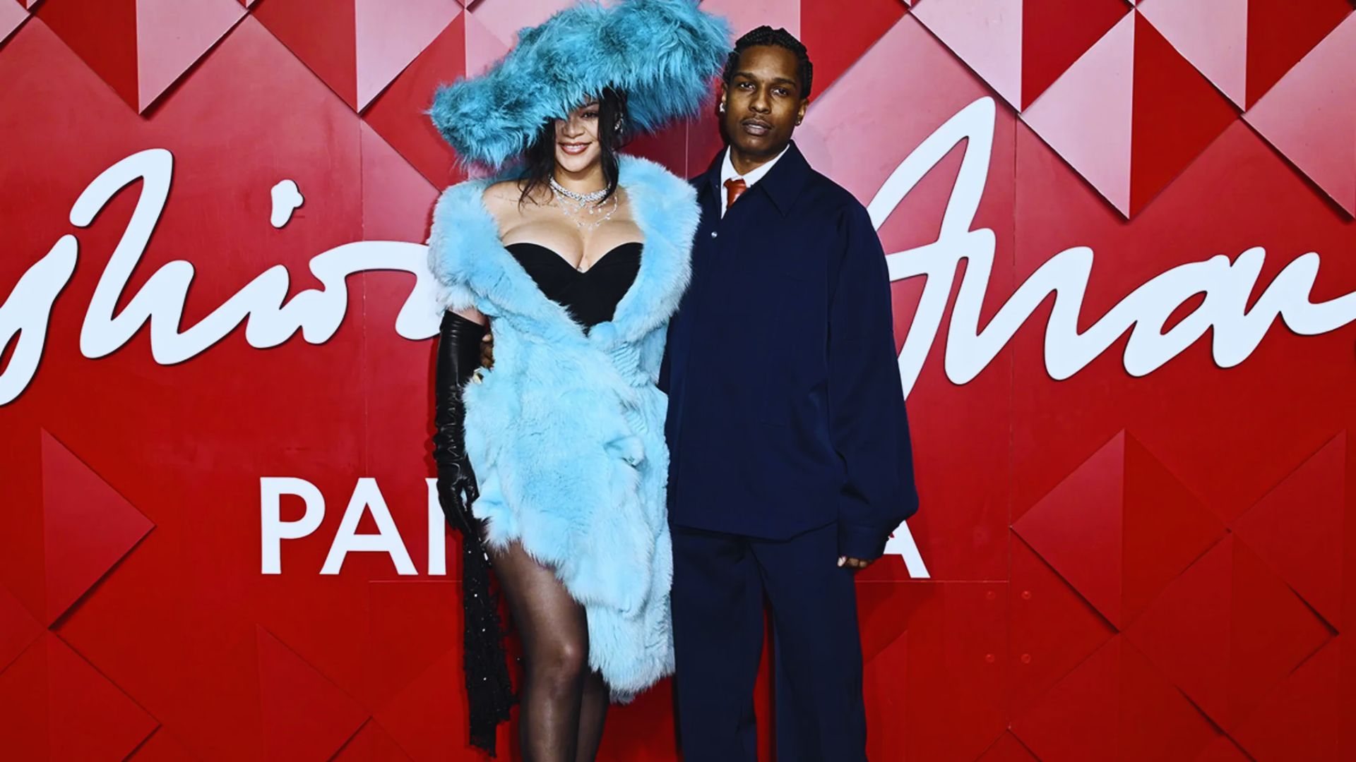 . A man and woman stand side by side, dressed elegantly, at a vibrant fashion show event.