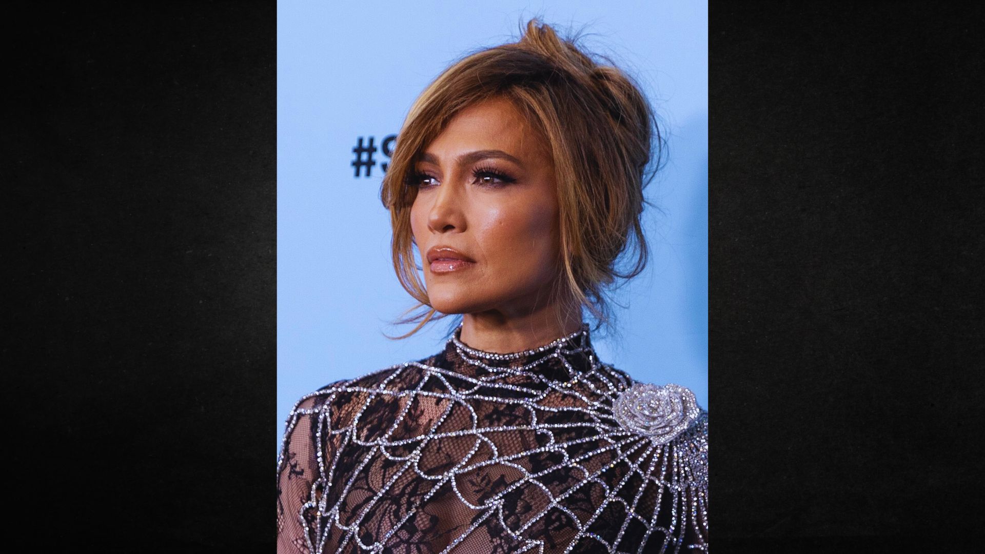 A woman with an elegant updo gazes thoughtfully off-camera. She wears a black dress adorned with intricate, shimmering beadwork, conveying sophistication.