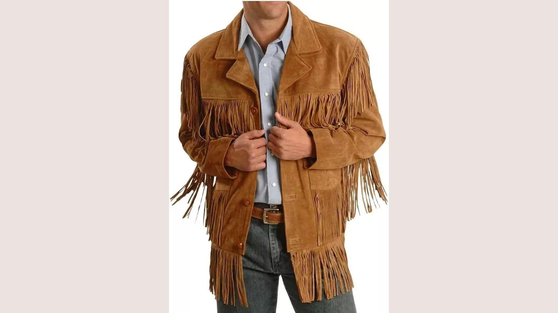 Man wearing a brown suede jacket with fringe details, over a light blue shirt and jeans, evoking a western style. Hands adjusting jacket.