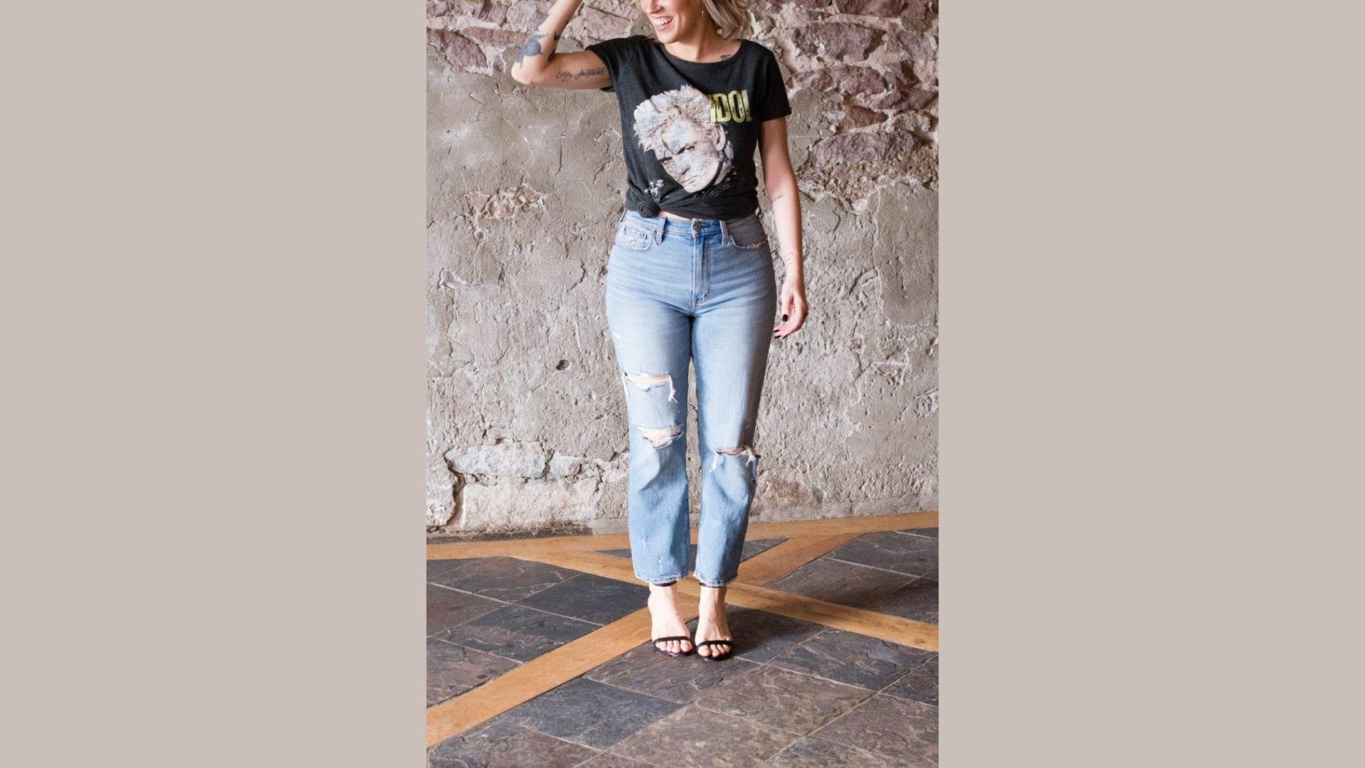 A woman dressed in ripped jeans and a t-shirt stands confidently, showcasing a casual and trendy outfit.