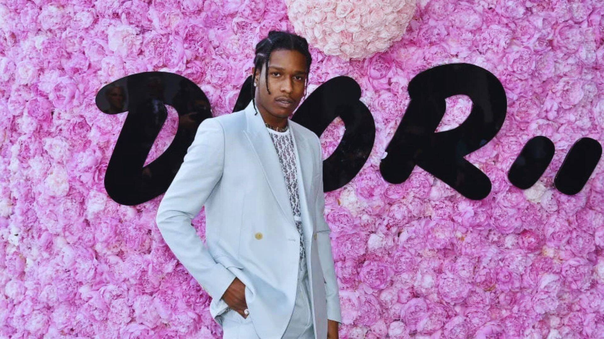 A man in a suit stands confidently in front of a vibrant pink wall.