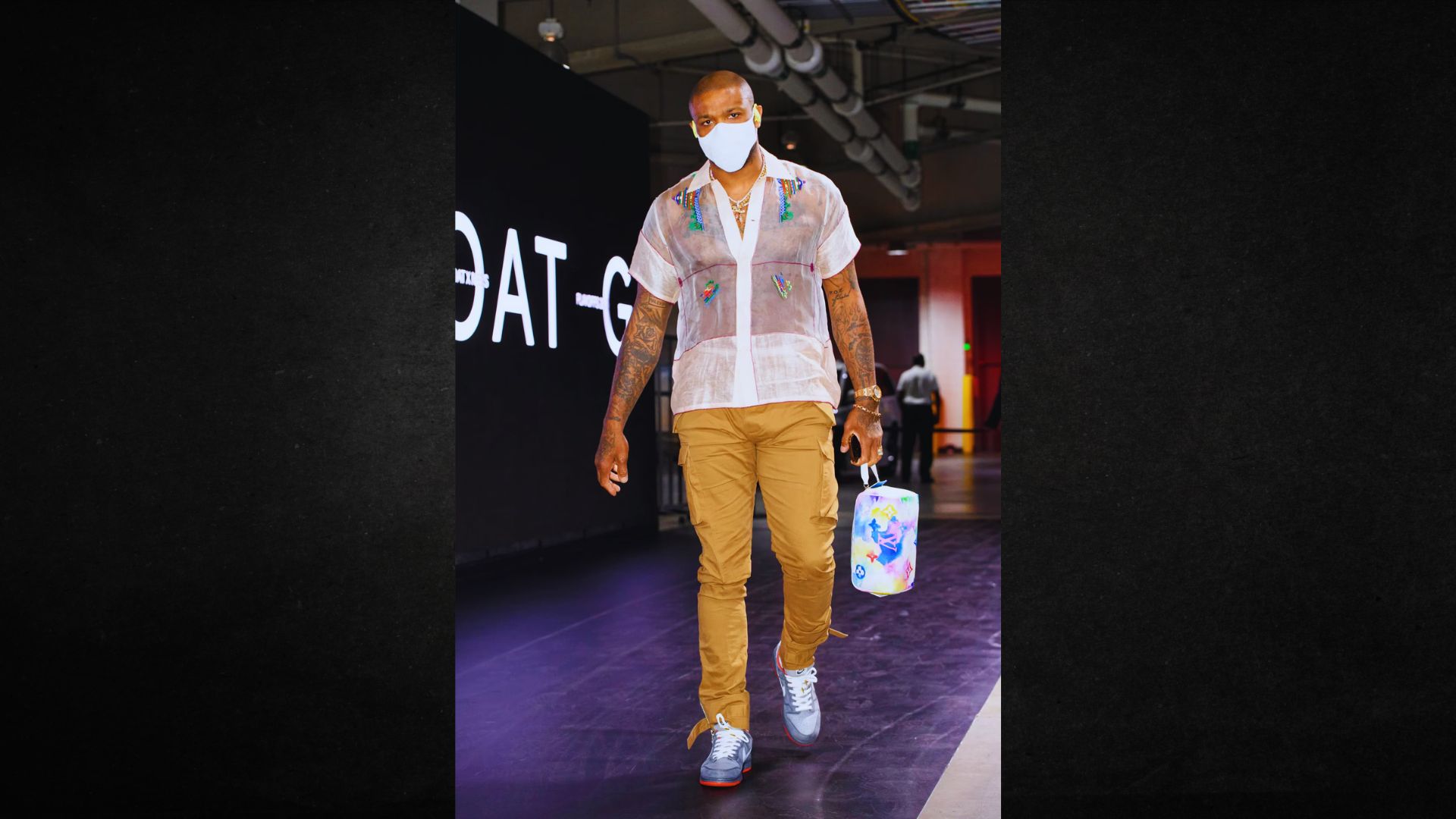 J A man in a white shirt and brown pants confidently walks down the runway, showcasing a fashion design.