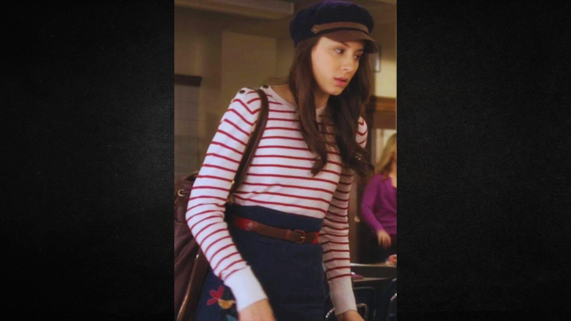 A woman wearing a striped shirt and a blue skirt stands confidently, showcasing her stylish outfit.