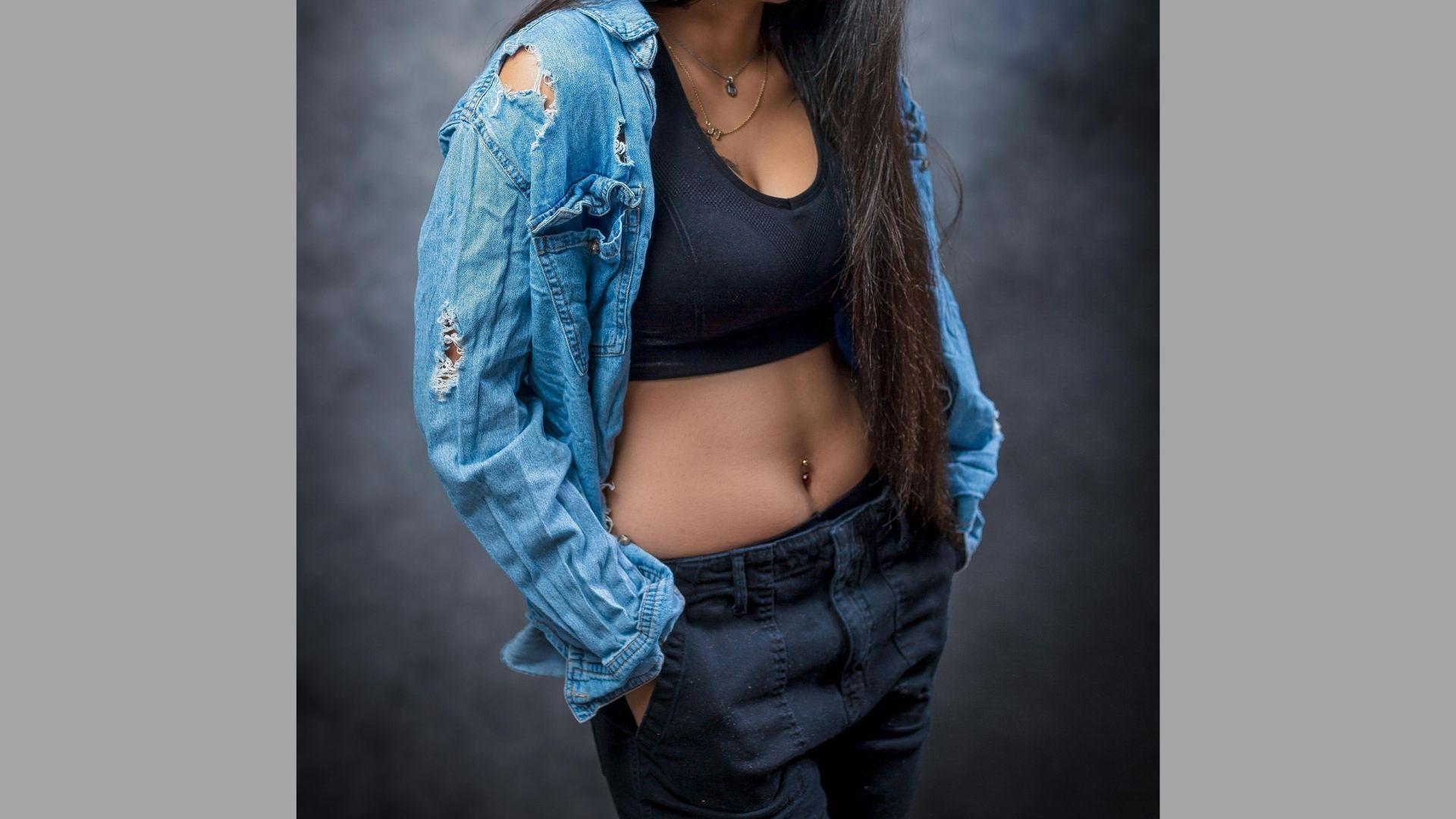 A woman wearing a denim jacket and black pants stands confidently, showcasing a casual yet stylish outfit.