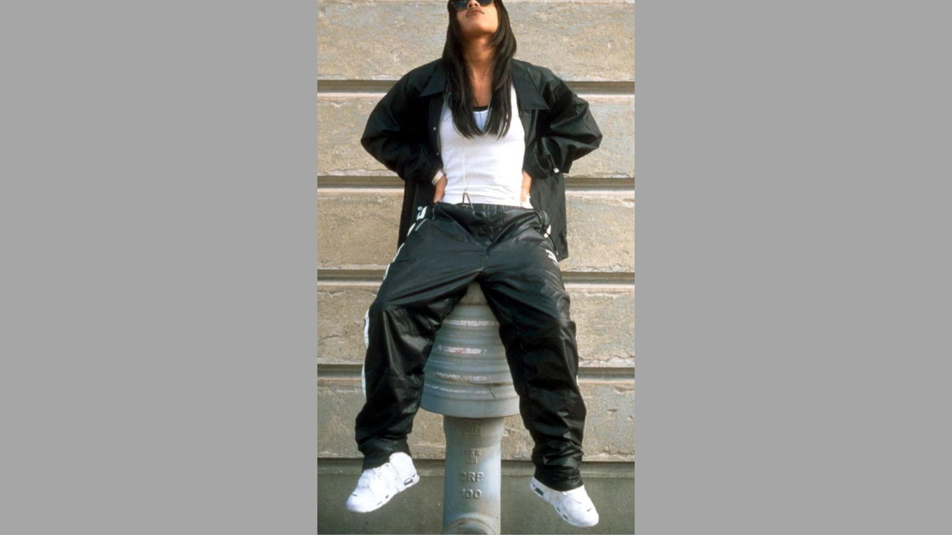 A man casually sitting on a fire hydrant in an urban setting, wearing casual clothes and smiling at the camera.