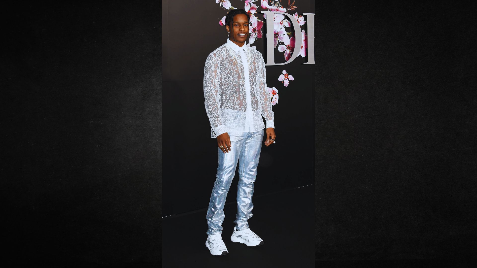A man wearing a white shirt and silver pants stands confidently, showcasing a modern and stylish outfit.