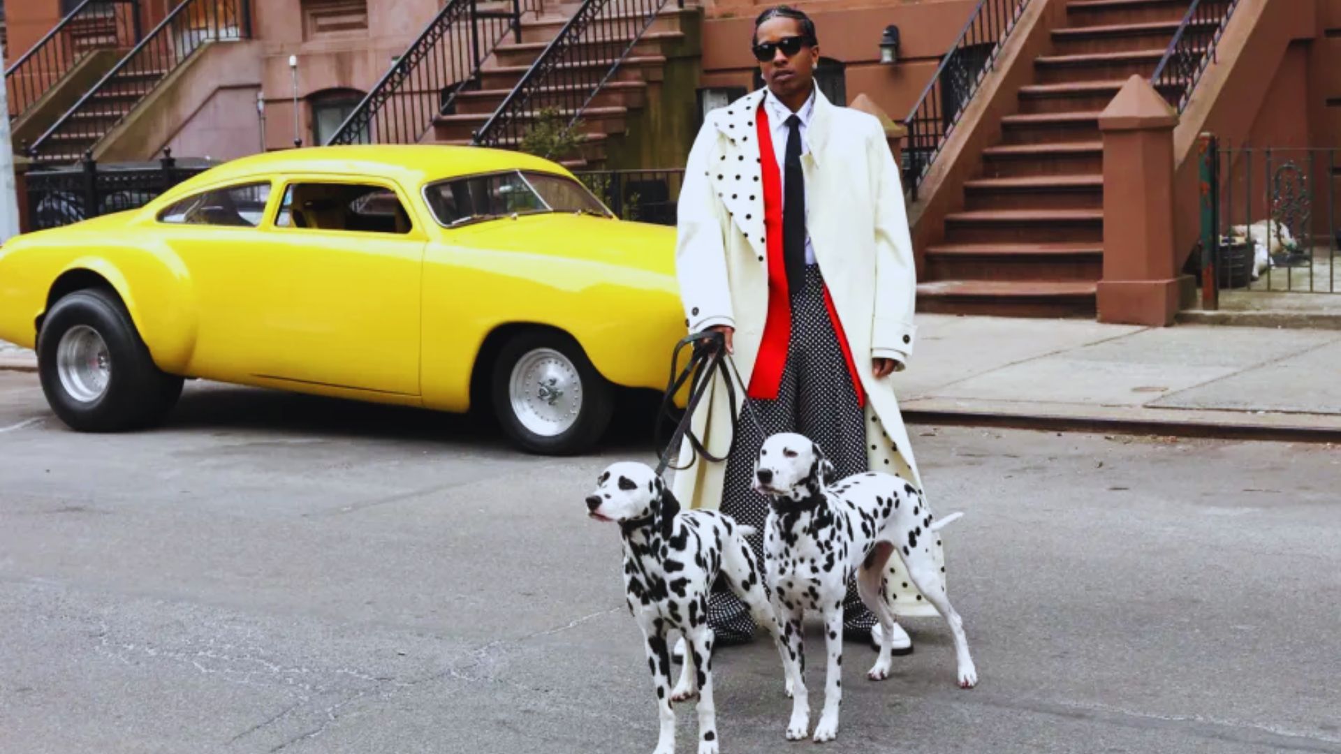 A person in a stylish white coat stands confidently with two Dalmatians on a city street, a bright yellow vintage car parked nearby.