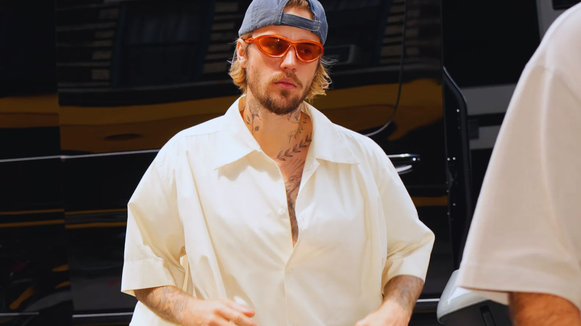 A man wearing a hat and sunglasses strolls down the street, enjoying a sunny day.