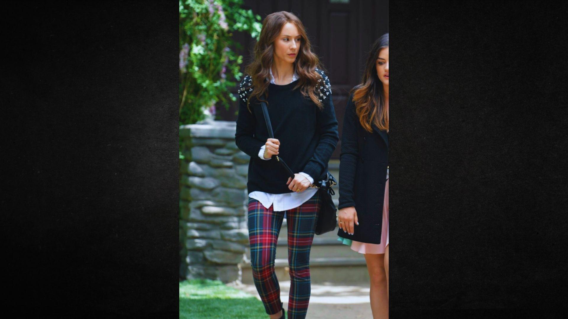 Two women wearing plaid pants and black sweaters stand together, smiling in a casual setting.