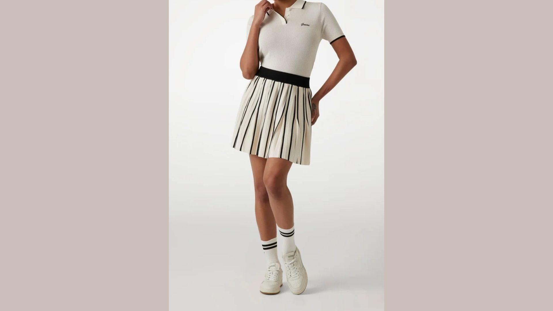 A woman wearing a white shirt and skirt stands confidently, showcasing a simple yet elegant outfit.