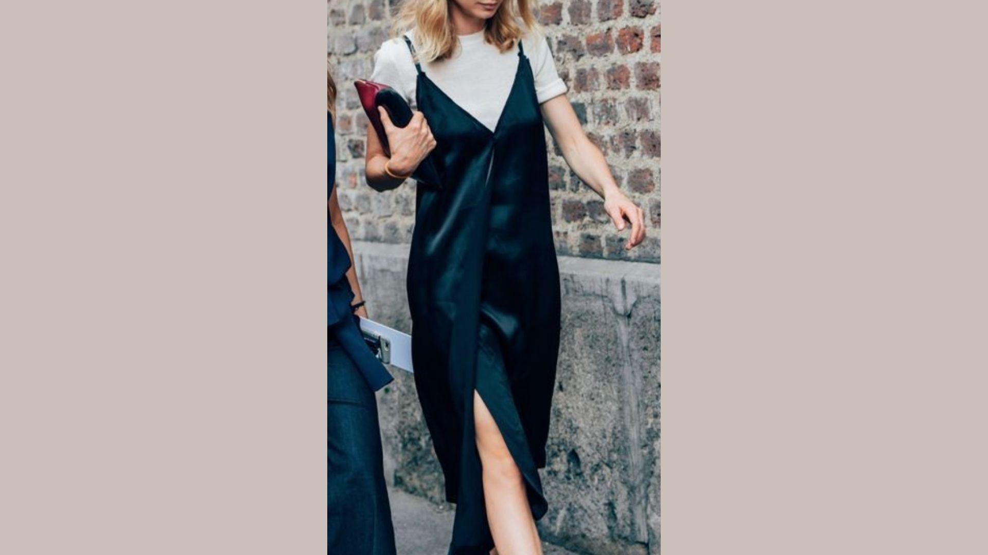 A woman in a black dress and heels confidently walks down the street, surrounded by urban scenery