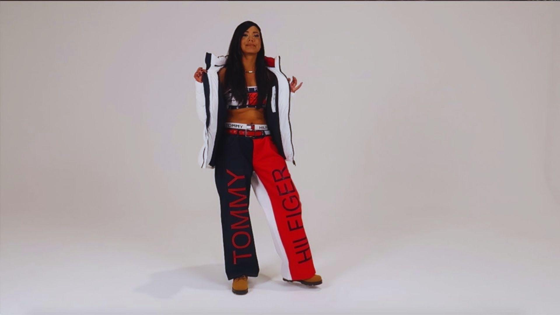 A woman in a white puffer jacket and color-blocked Tommy Hilfiger pants poses confidently against a plain backdrop, exuding a sporty, stylish vibe.