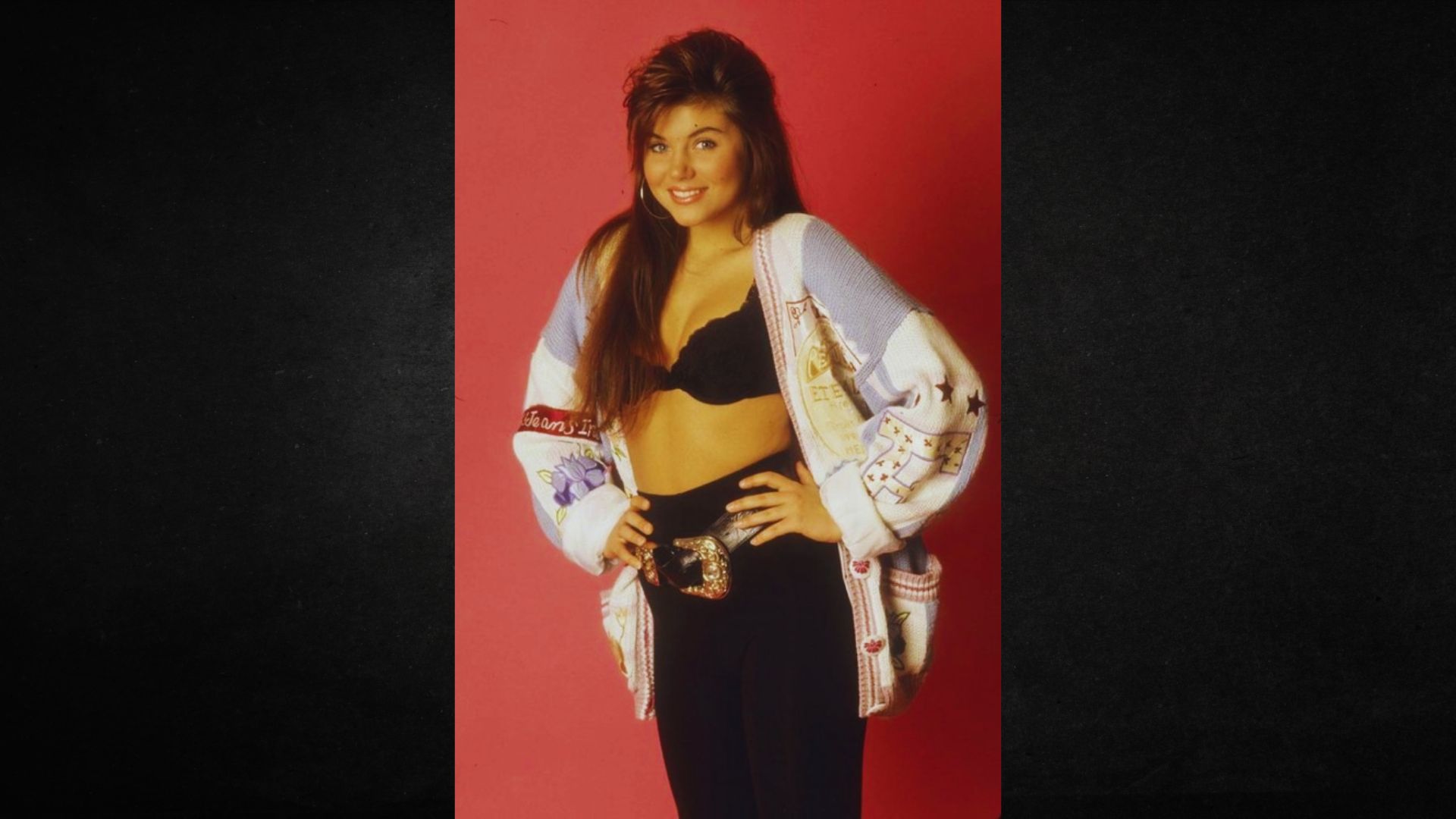 A woman wearing a black top and a white jacket stands confidently, showcasing a stylish outfit.