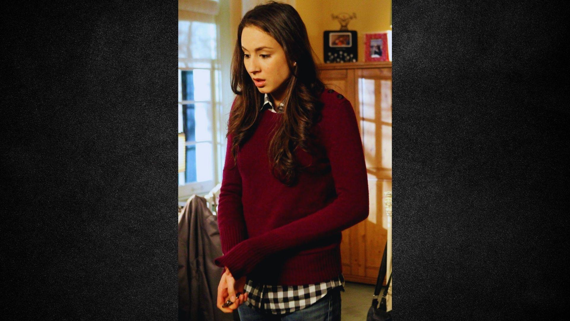 A woman in a red sweater is positioned in a cozy room, appearing relaxed and engaged.