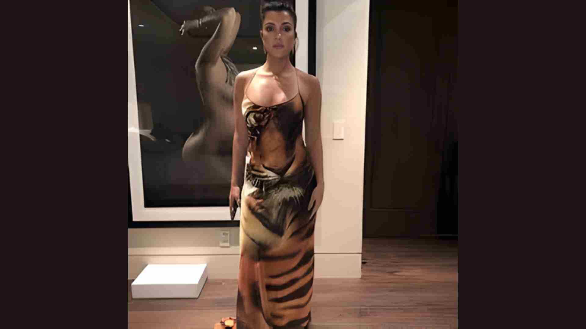 Woman in a dress with a tiger print design stands in a dimly lit room, exuding elegance. A blurred, artistic photograph of a person is on the wall behind her.