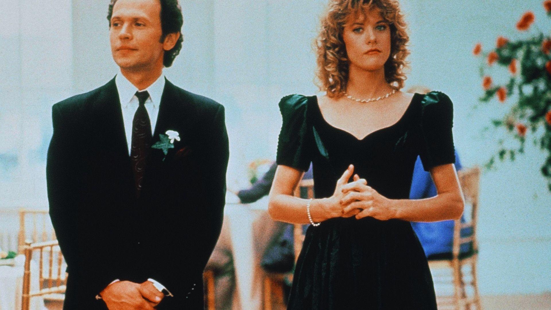 A man and woman in formal attire stand side by side, both smiling and looking towards the camera.