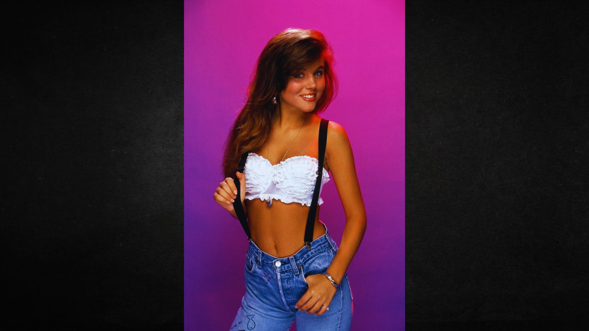 A woman wearing a white top and blue jeans stands confidently, smiling at the camera.