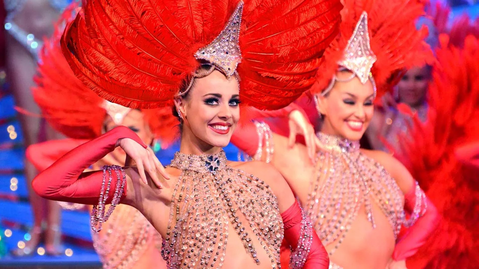 A woman adorned in vibrant red feathers and a matching headdress, embodying a Moulin Rouge-influenced outfit.