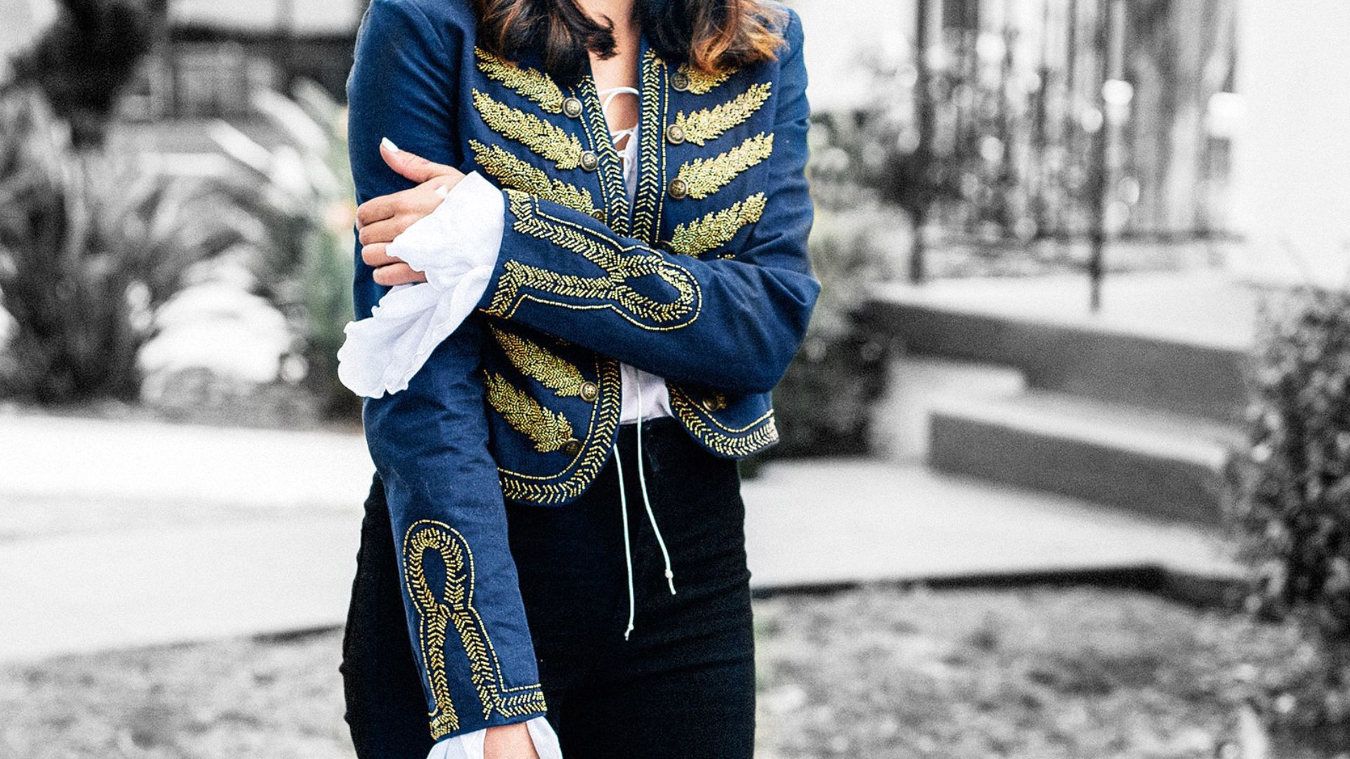 A woman wearing a blue jacket and black pants stands confidently, showcasing a casual yet stylish outfit.