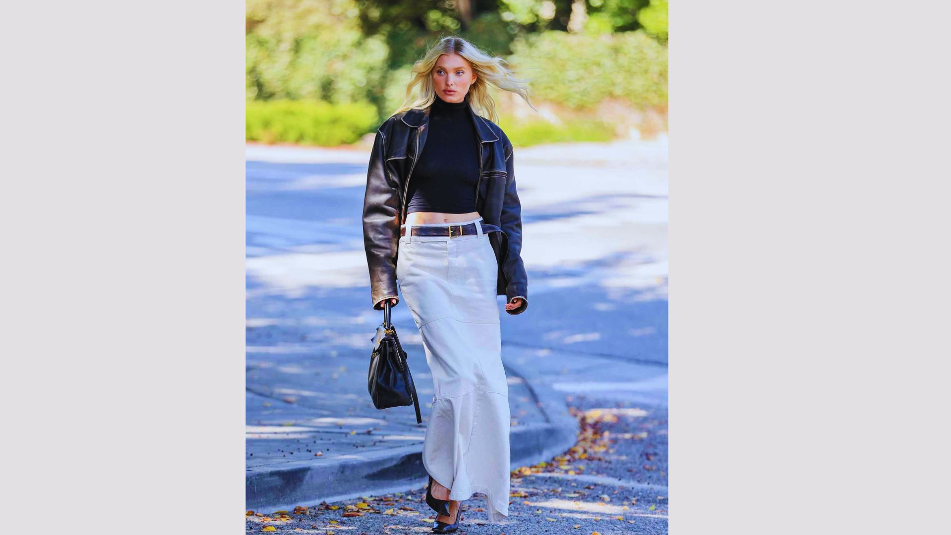 A woman wearing a black top and white skirt strolls along the street.