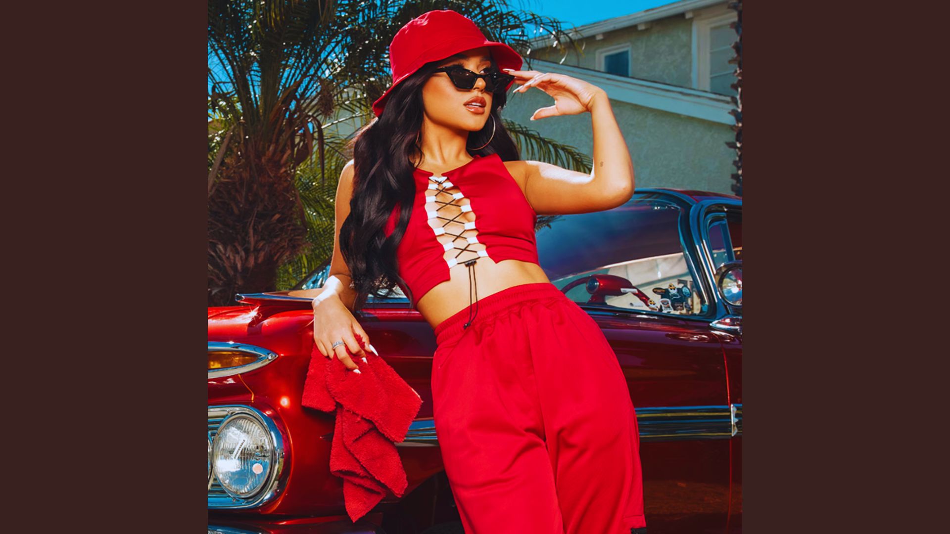 A woman in a red outfit poses confidently beside a classic car, showcasing a stylish and vibrant scene.