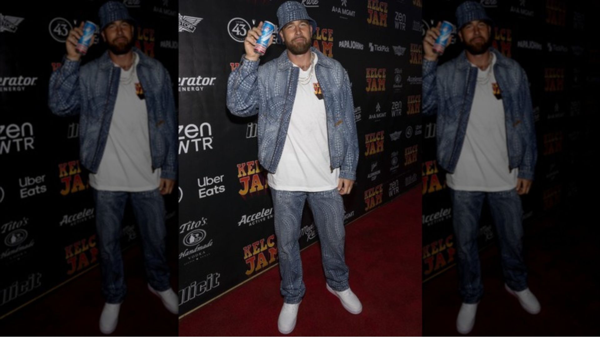 3. A man dressed in a blue jacket and jeans stands on a bold red carpet.