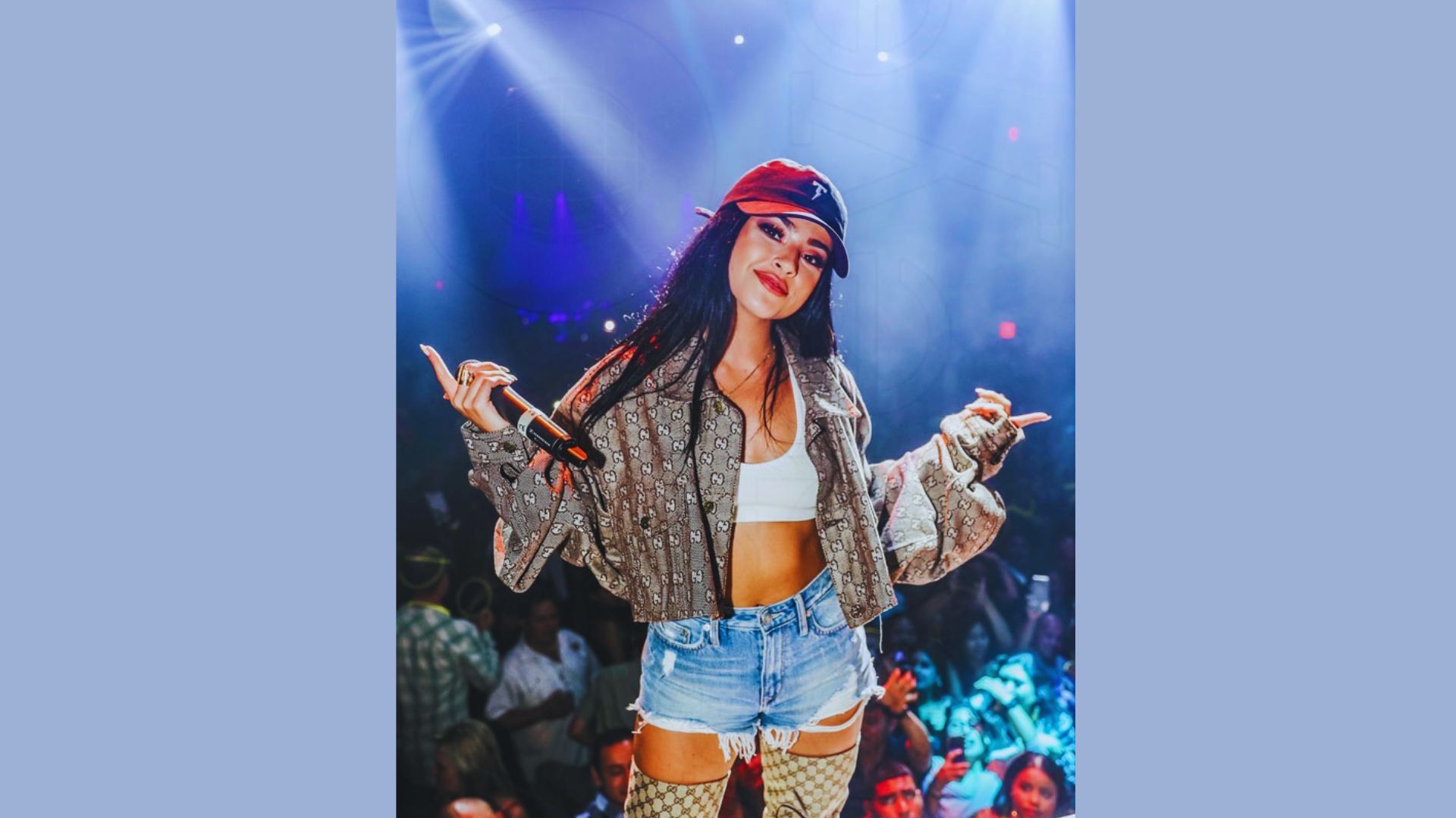 A woman wearing a hat and shorts stands confidently on stage, engaging with the audience.