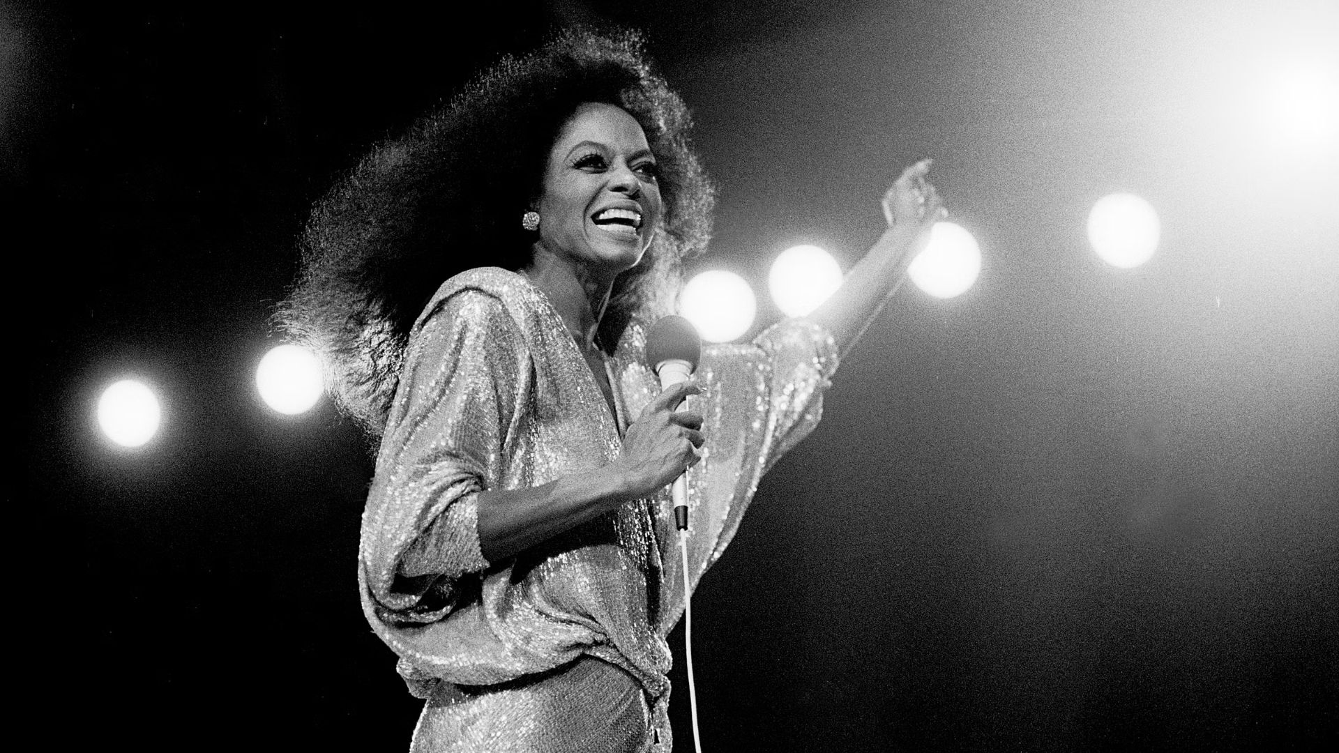 2. A woman wearing a shimmering sequin dress performs a song into a microphone, captivating the audience.