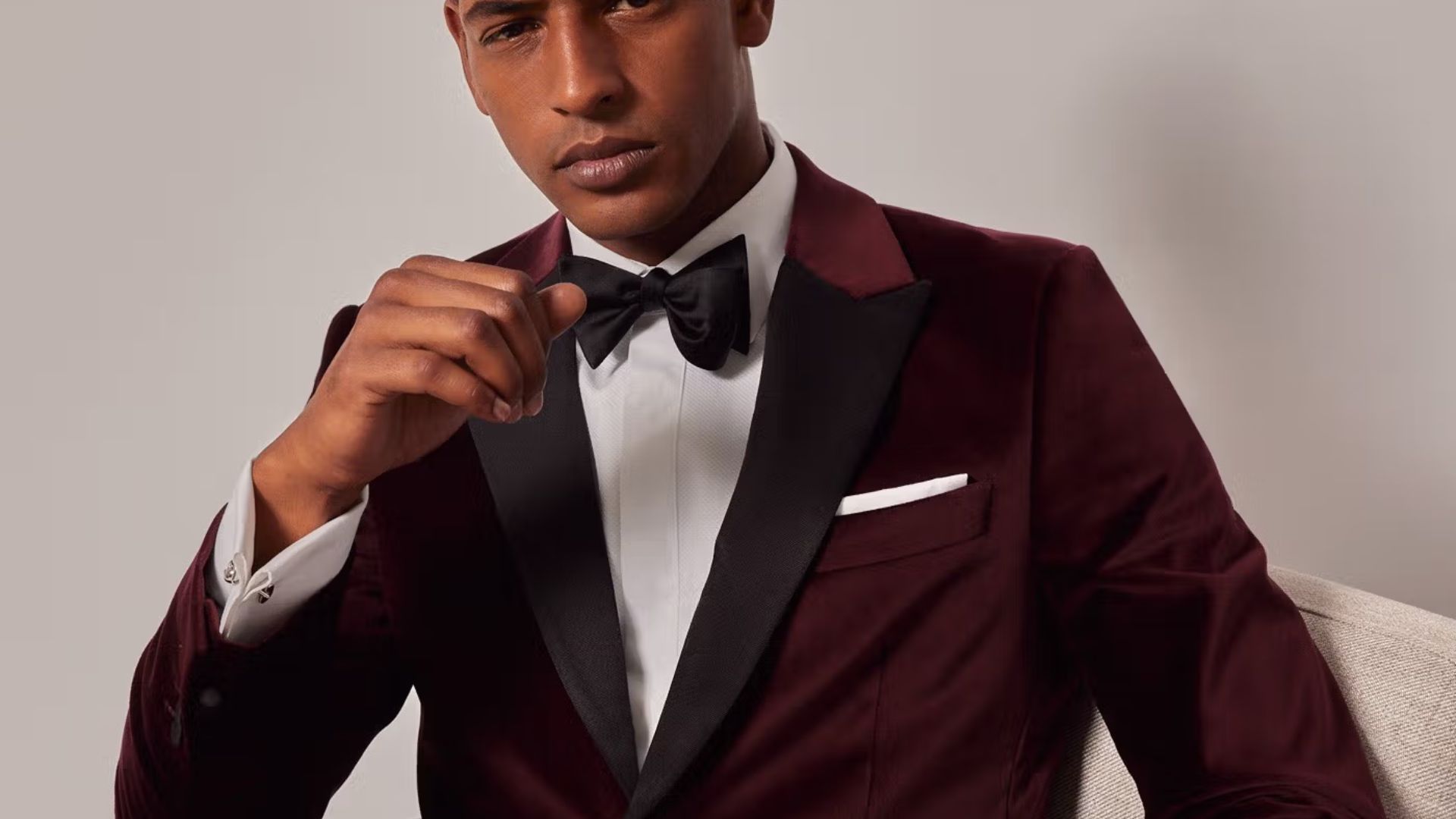 A man wearing a burgundy suit and bow tie, showcasing a stylish party outfit for a Saltburn event.