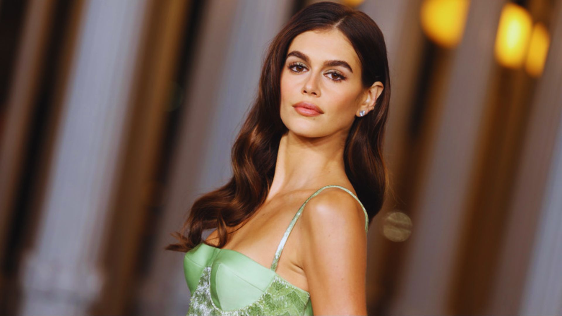 A woman in a green dress poses confidently for the camera, smiling and looking directly at the viewer.