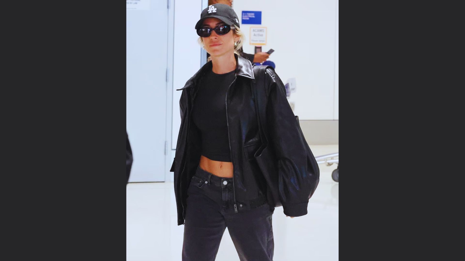 A woman wearing a black leather jacket and jeans stands confidently, showcasing a stylish and edgy look.