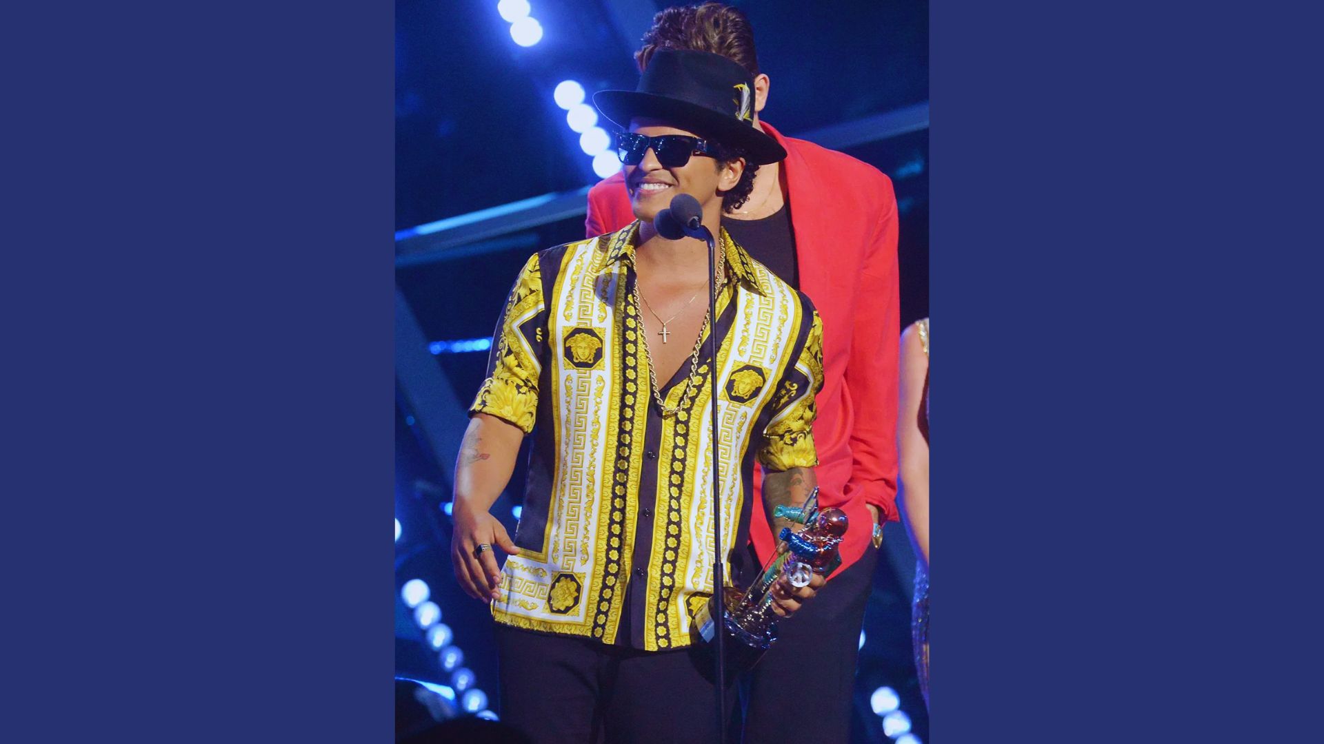 Bruno Mars in a yellow shirt with a black hat on his head, probably giving a winning speech.