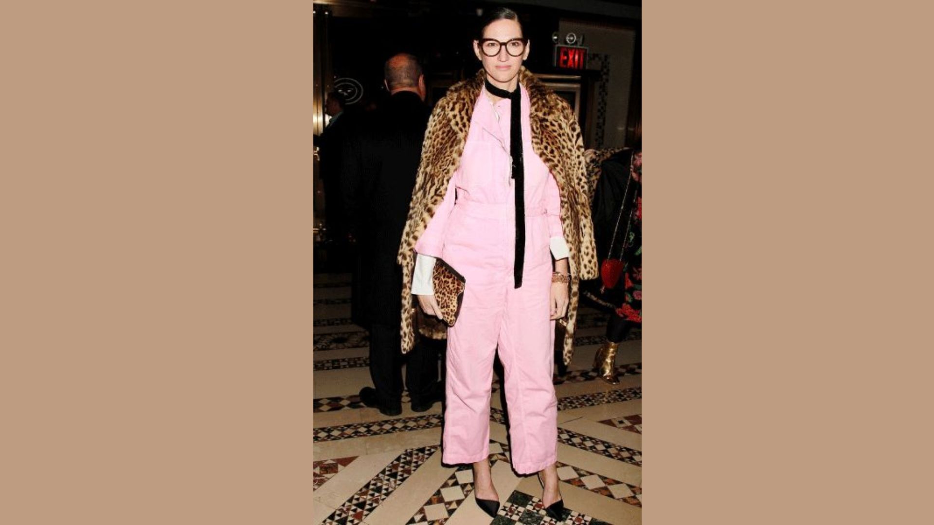 A woman wearing a pink suit and a leopard print coat stands confidently, showcasing a bold fashion statement.