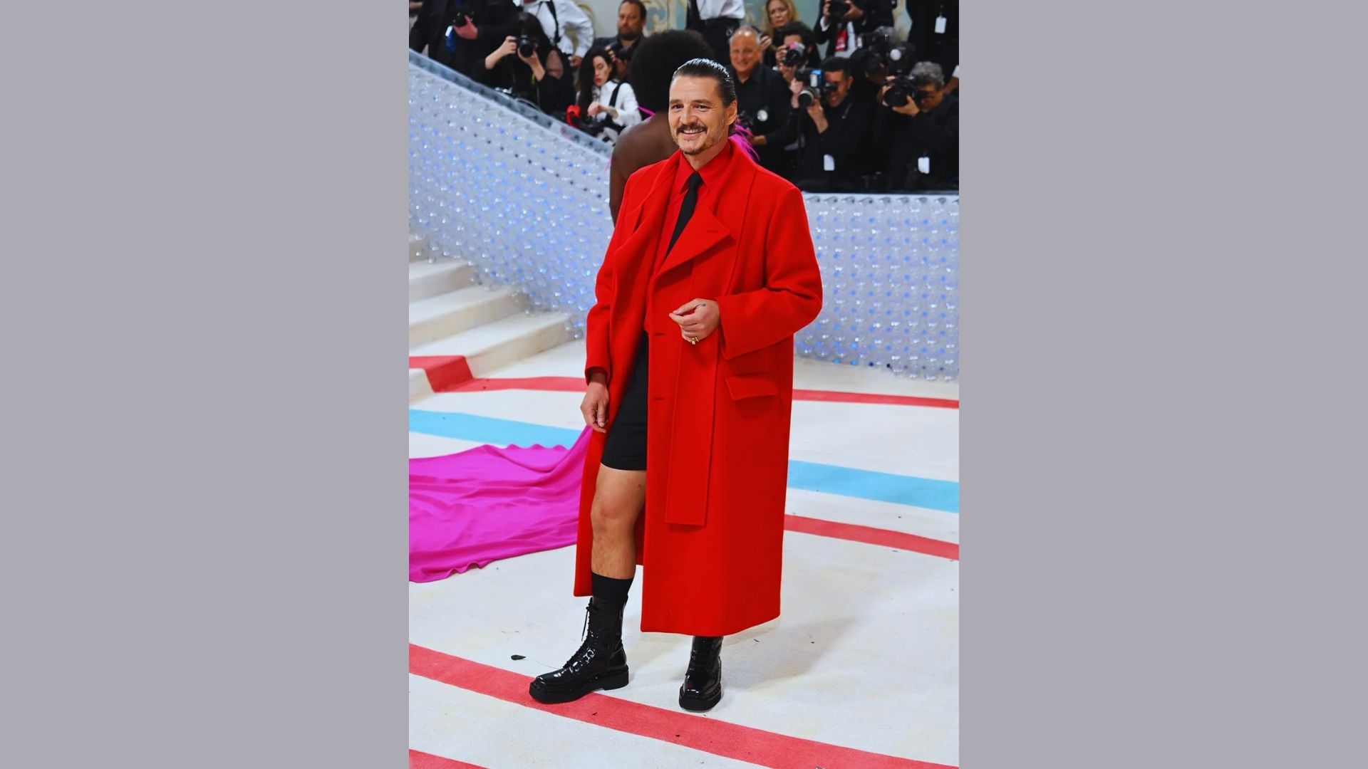 A man wearing a red coat and black boots stands confidently, showcasing a stylish and bold fashion choice.
