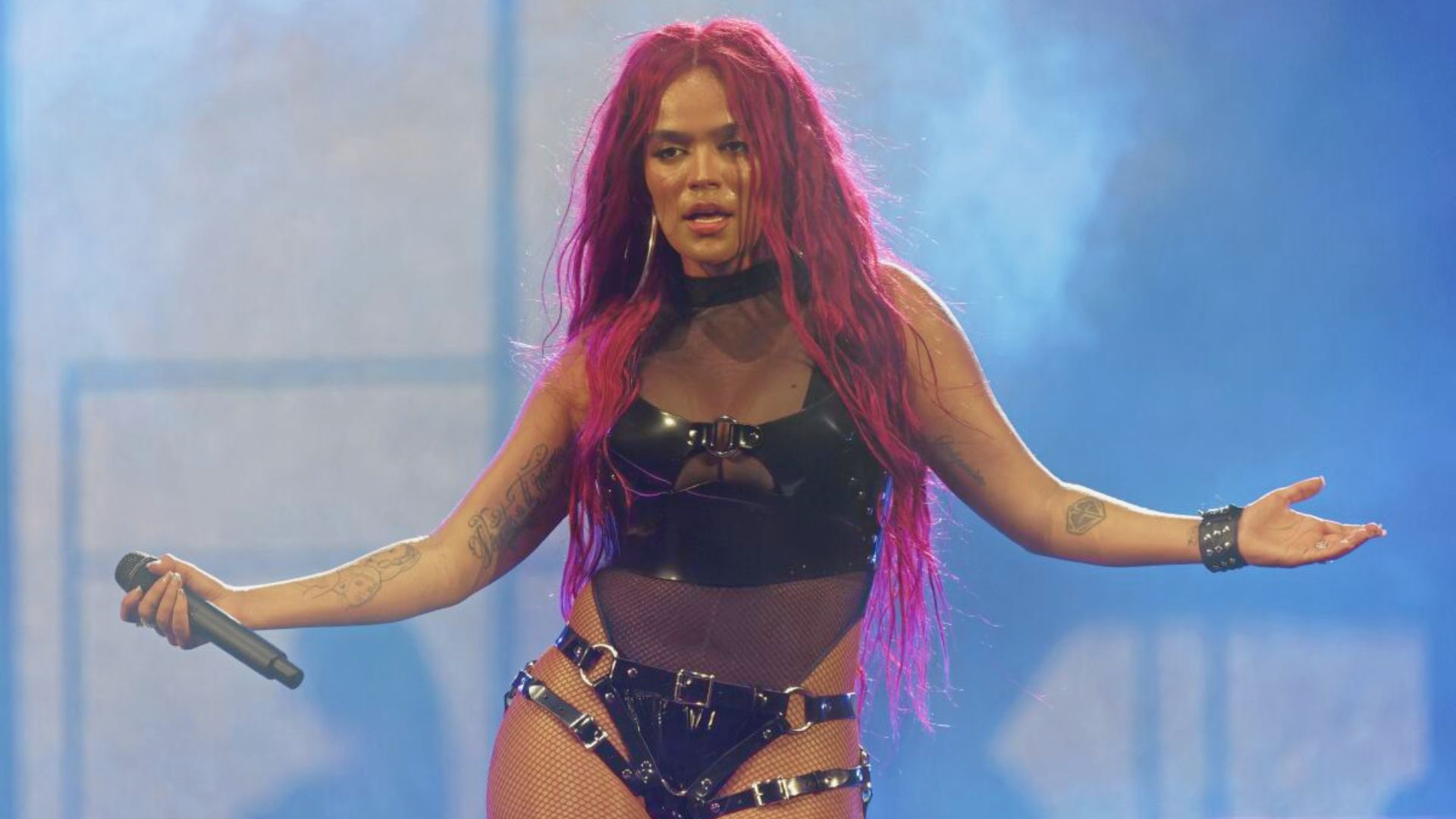 A woman with pink hair wearing a black outfit performs on stage, engaging the audience with her presence.