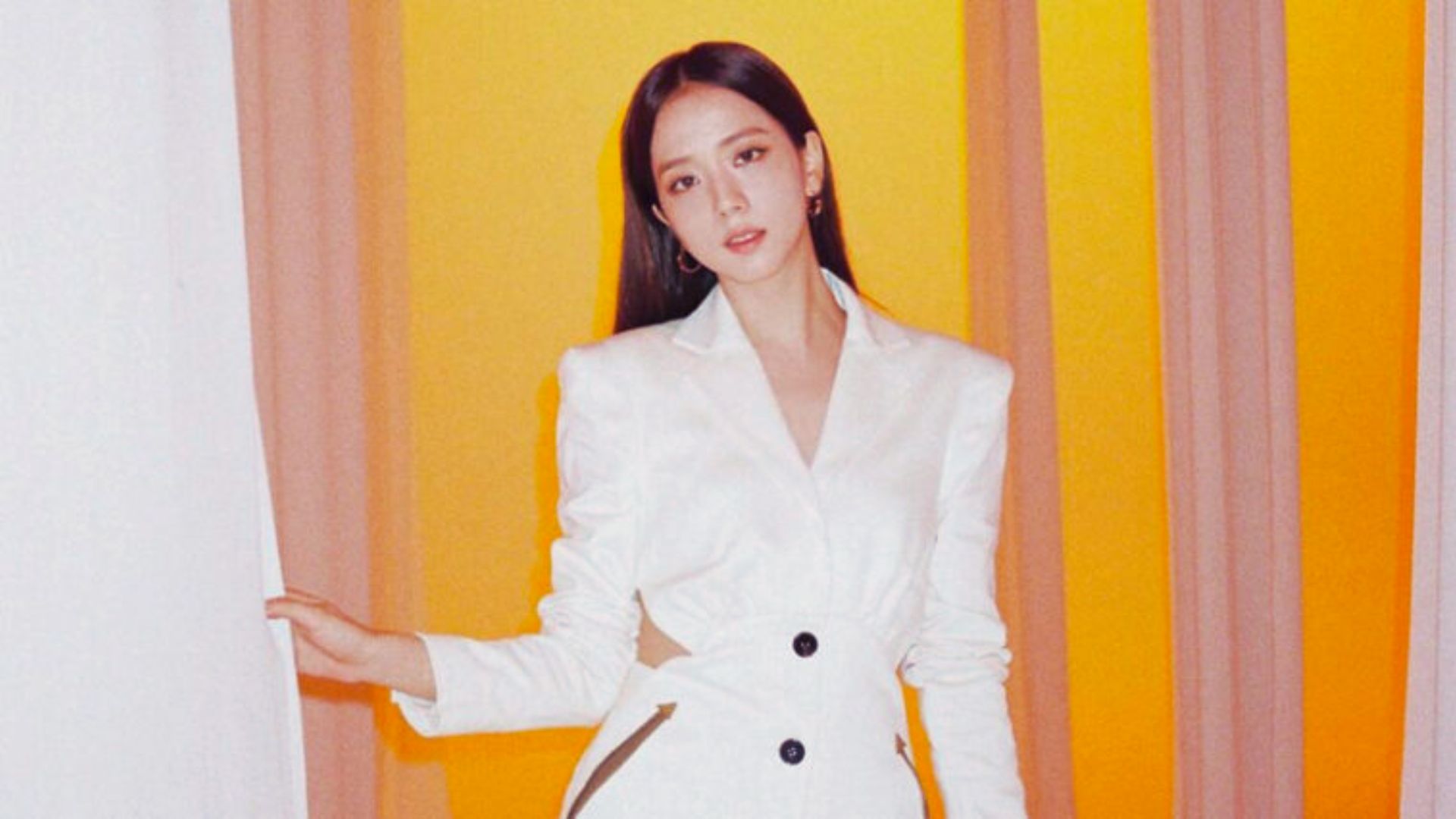 A woman wearing a white suit and black shoes stands confidently, showcasing a professional appearance.