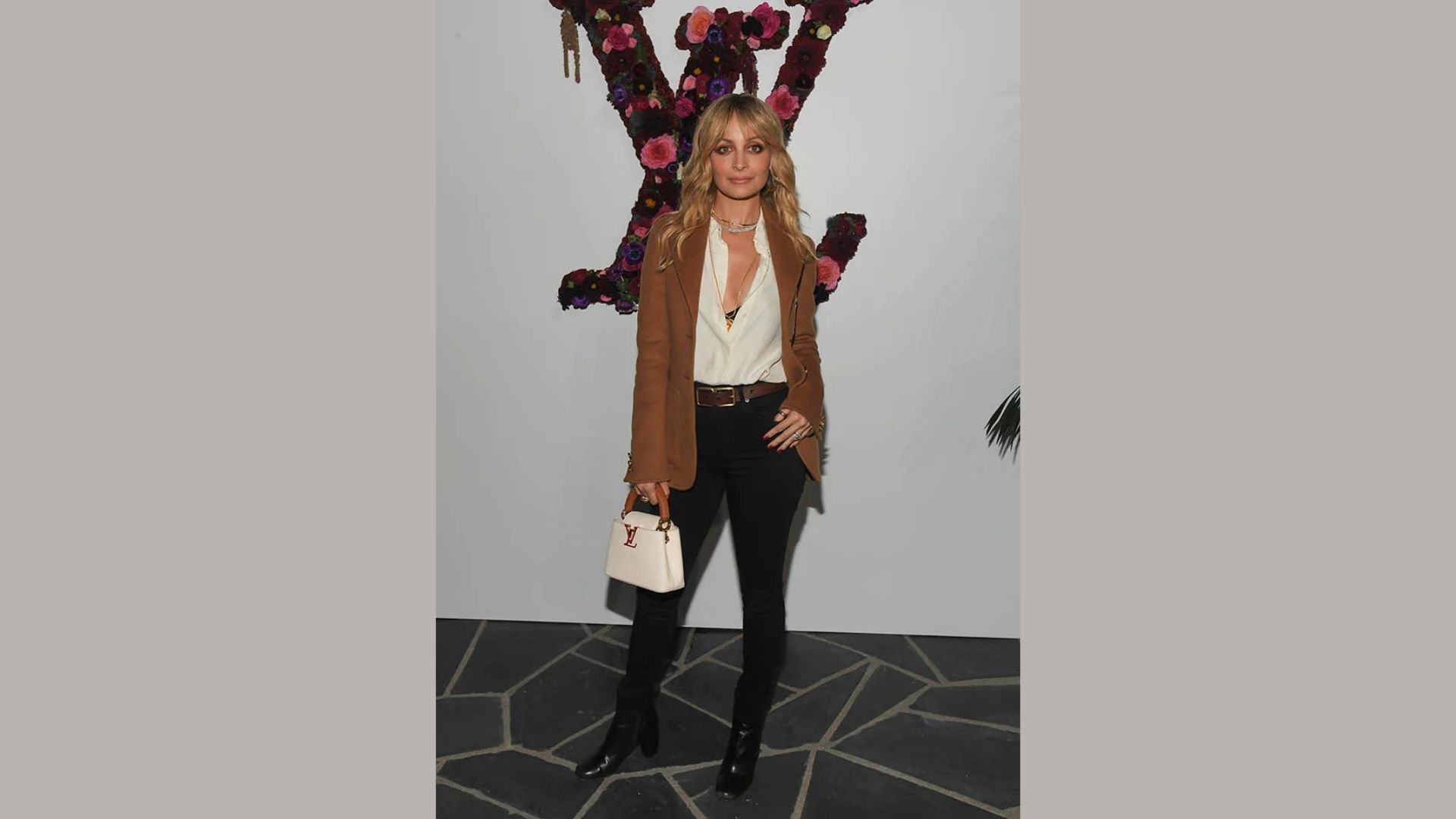 A woman wearing a brown blazer over a white shirt, styled with high-rise denim and ankle boots for a fall look.