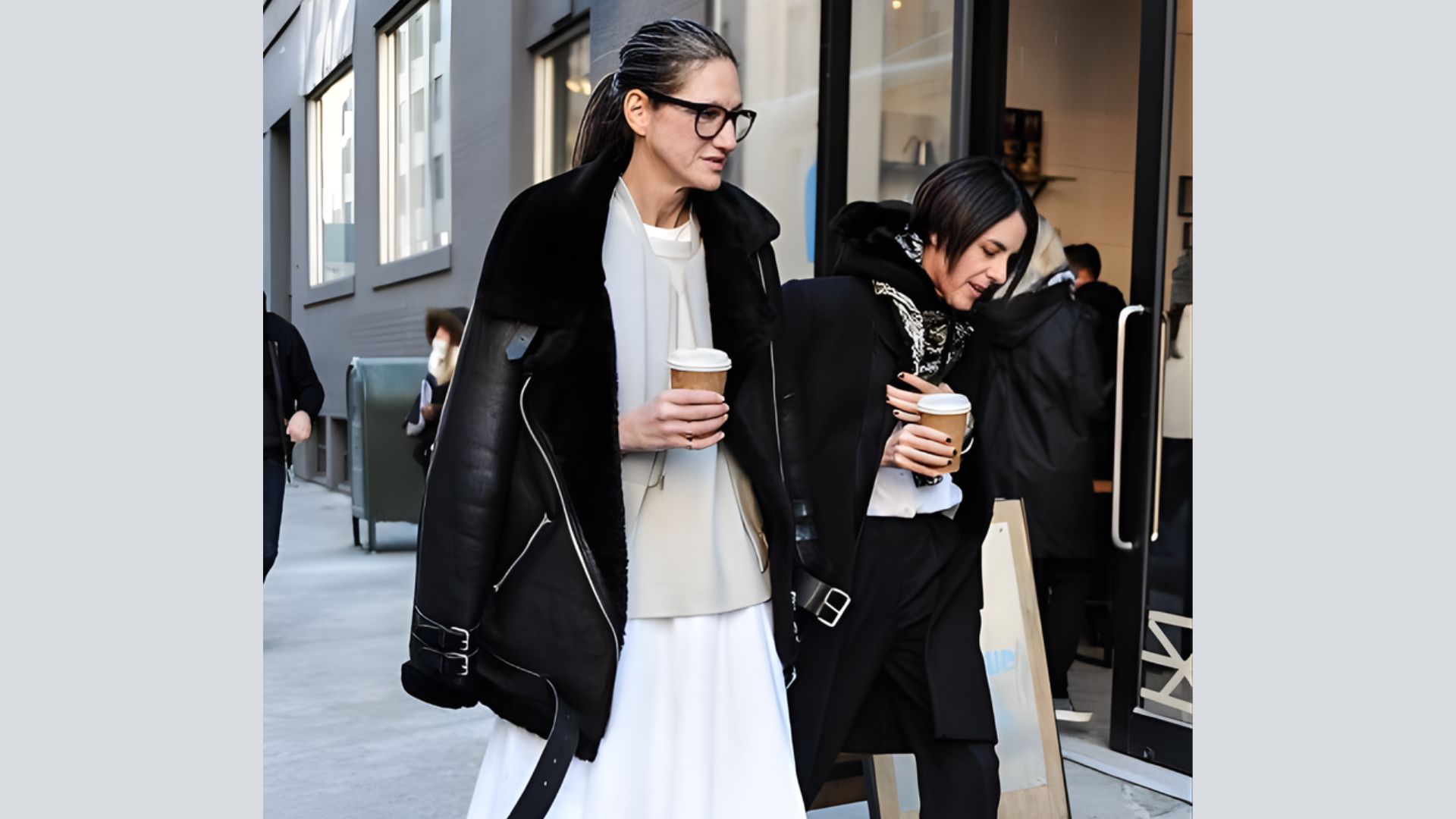 Two women stroll down the street, each holding a cup of coffee, enjoying their time together.