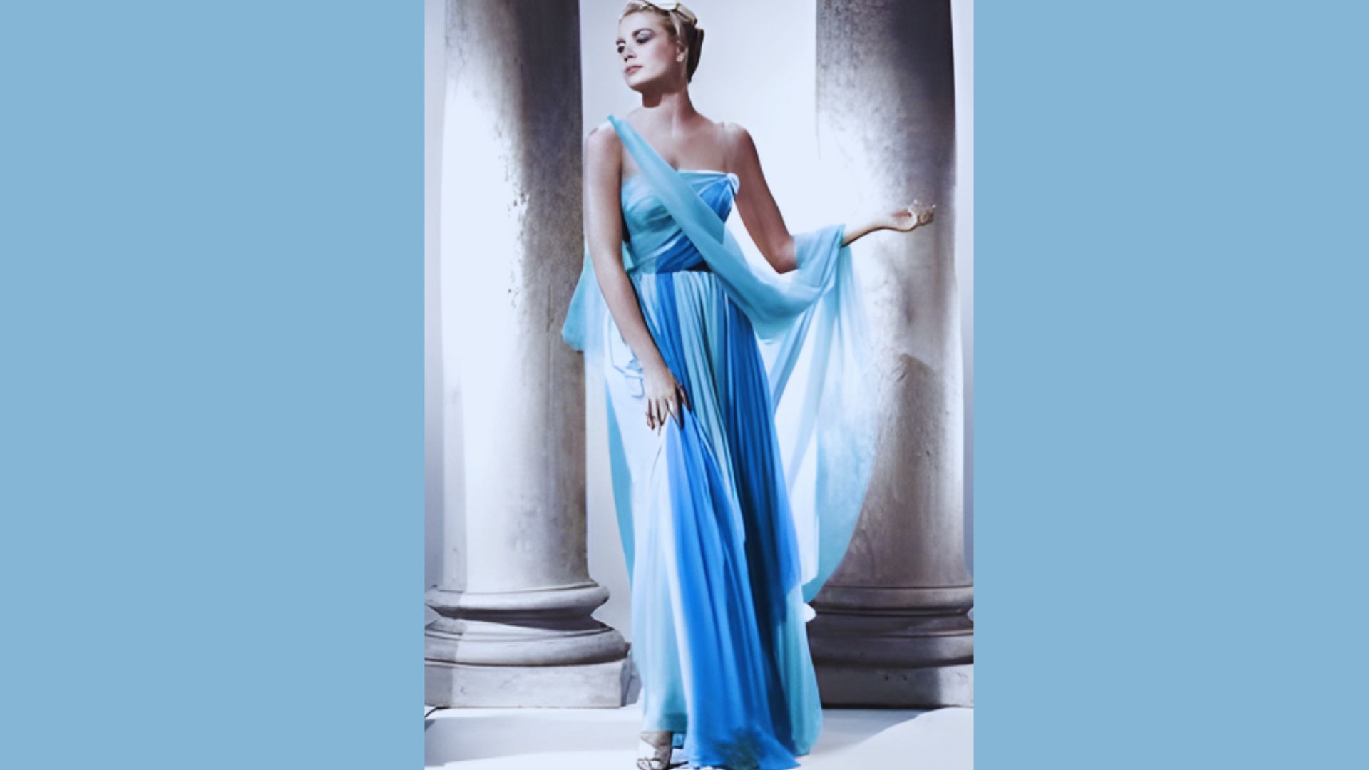 1. A woman in a blue dress stands gracefully in front of tall, classical columns.