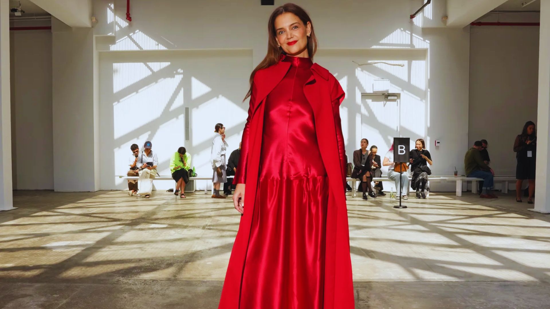 A woman wearing a vibrant red dress walks the runway, highlighting the latest trends in fashion with confidence.