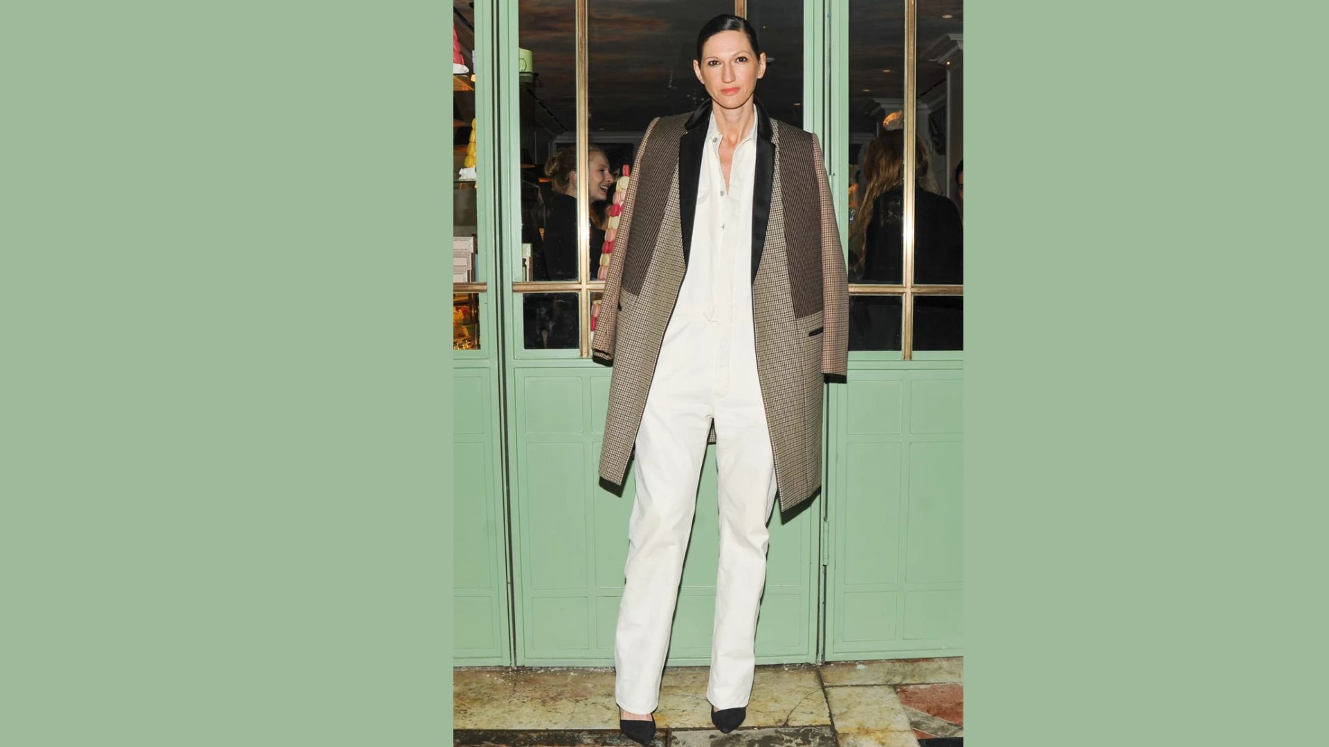 A woman wearing white pants and a coat stands confidently, showcasing a stylish and modern outfit.