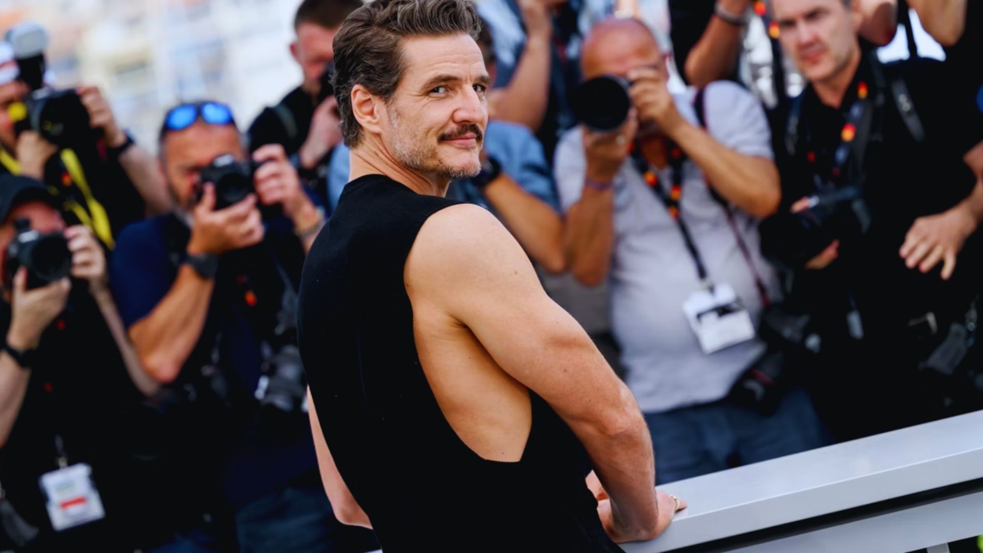 A shirtless man stands confidently in front of a large crowd, engaging with the audience.