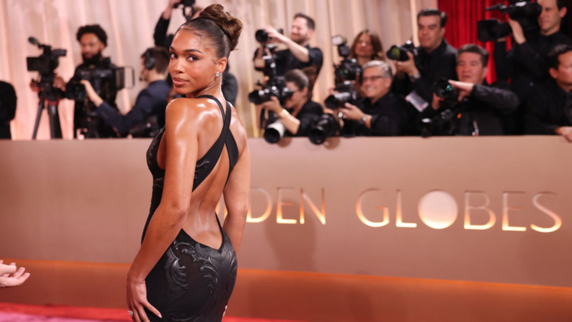A woman in an elegant black dress poses confidently on the red carpet at a glamorous event.