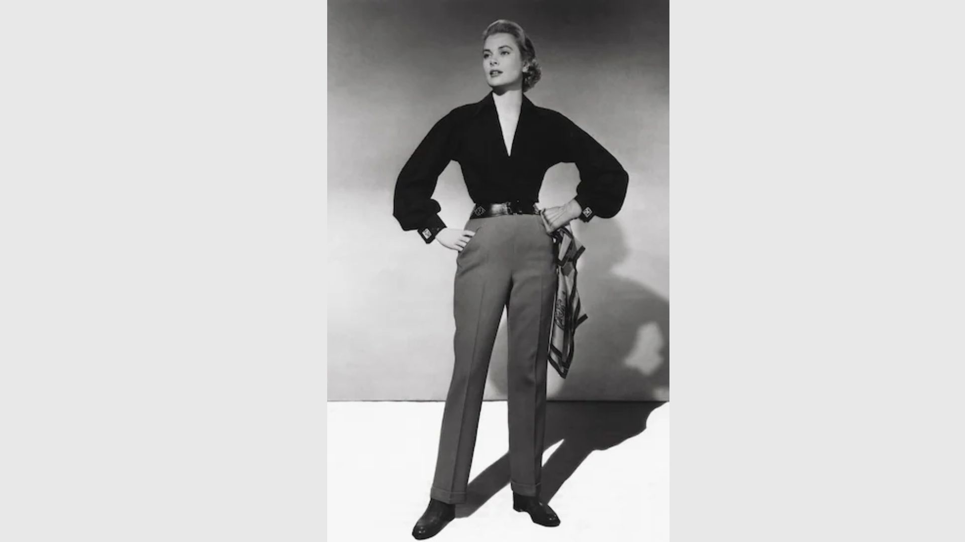 1. A woman wearing a black top and grey pants stands confidently, showcasing a casual yet stylish outfit.