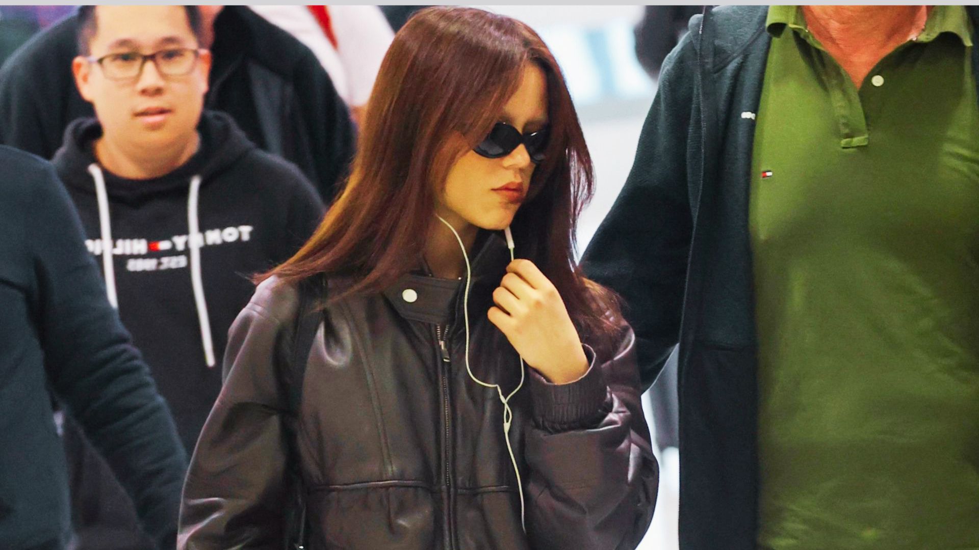 A woman in sunglasses and a black leather jacket, accessorized with bold statement pieces.