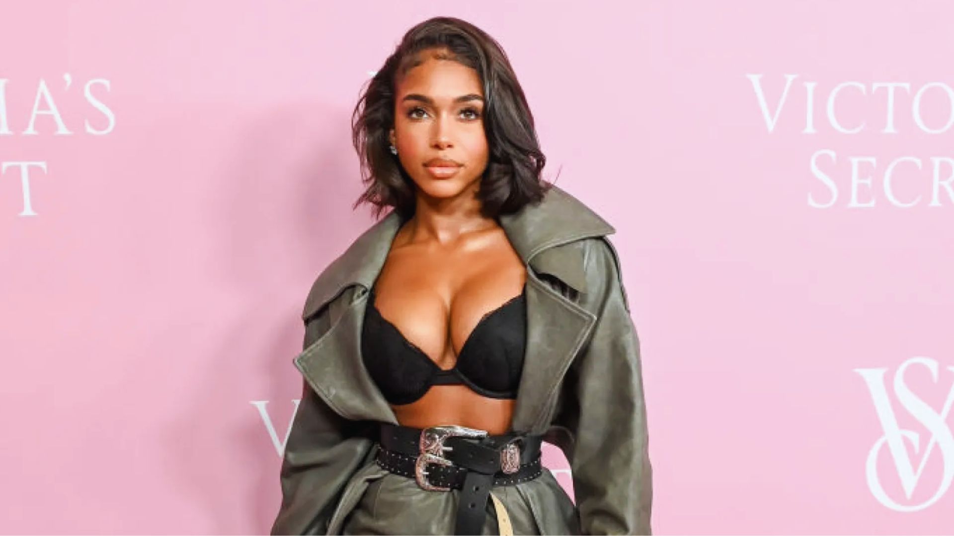 A woman wearing a leather jacket over a black bra, posing confidently against a neutral background.